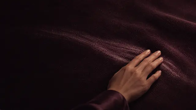 Une main glisse lentement sur un velours mauve et y laisse une trace plus claire.
